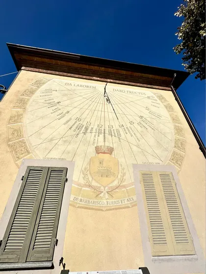 Inquadratura dal basso di una grande meridiana decorata, dipinta sulla facciata di un edificio sotto un cielo azzurro e limpido.