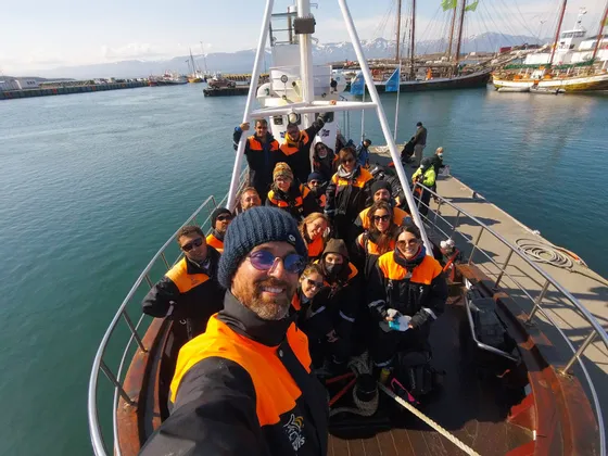 Eine WeRoad-Gruppe in orangen Schwimmwesten posiert für ein Selfie an Deck eines Bootes im Hafen.