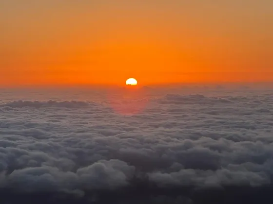 Il sole arancione brillante tramonta all'orizzonte sopra una densa coltre di nuvole bianche e grigie, visto dall'alto.