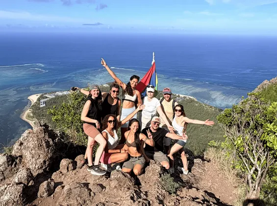 Un voyage de groupe WeRoad posant ensemble sur un sommet de montagne avec une vue panoramique sur l'océan bleu et le littoral.