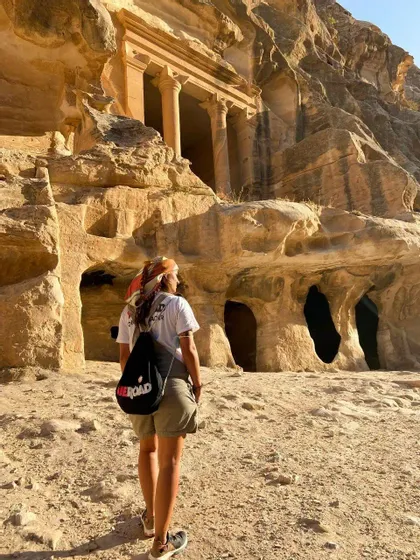 Eine Person, von hinten gesehen, mit einem WeRoad Rucksack, blickt zu einer antiken Fassade mit in einen Sandsteinfelsen gehauenen Säulen auf.