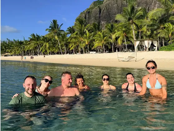 Un groupe WeRoad de sept personnes souriantes dans l'océan, face à une plage tropicale avec des palmiers.