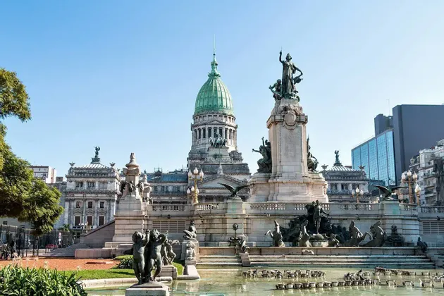 El Palacio del Congreso Nacional Argentino con su cúpula verde, visto desde una plaza con un gran monumento y fuente.