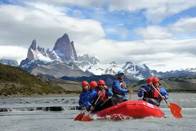 Un viaje en grupo WeRoad haciendo rafting en una balsa inflable roja en un río, con una gran cordillera nevada de fondo.