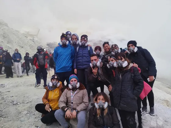 Eine WeRoad Reisegruppe posiert für ein Foto mit Atemschutzmasken in einer rauchigen, vulkanischen Umgebung.