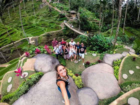 Eine Frau macht ein Selfie mit einer WeRoad-Gruppenreise, posiert zusammen auf einem Hügel mit Blick auf üppig grüne Reisterrassen und Palmen.