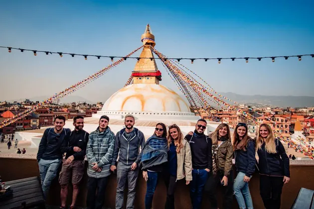 Un grupo de WeRoad posando en una azotea con una gran estupa blanca y banderas de oración de fondo.