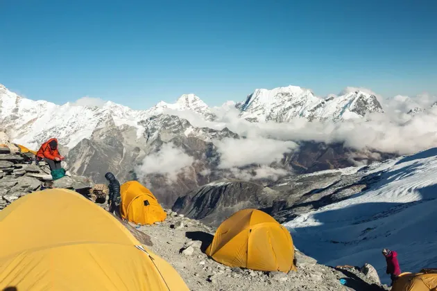Un grupo de WeRoad acampa en tiendas amarillas brillantes en una ladera rocosa, con una vasta cordillera de picos nevados al fondo.