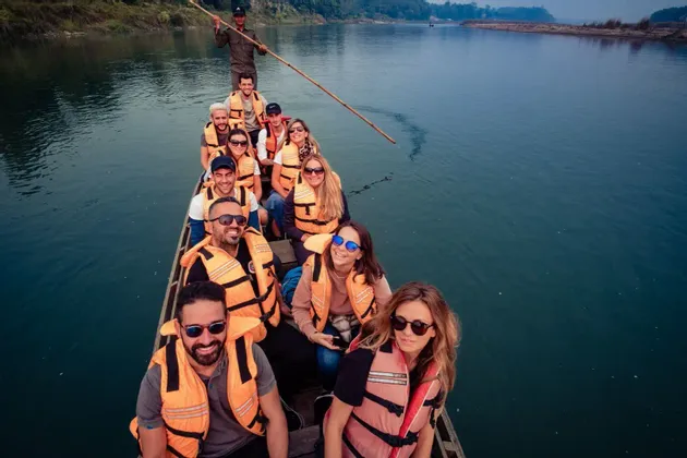 Un grupo de WeRoad con chalecos salvavidas naranjas a bordo de un largo bote de madera, mientras un guía lo impulsa por un río.