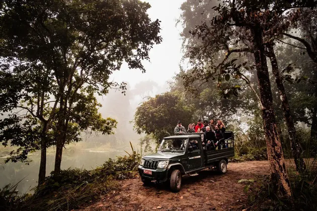 Eine WeRoad-Gruppe fährt in einem offenen Jeep auf einer Schotterstraße durch einen nebligen Wald am Fluss entlang.