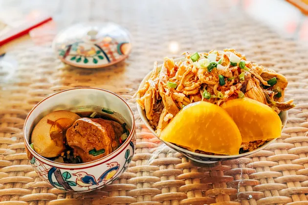 Deux bols de cuisine taïwanaise, l'un avec du poulet effiloché et du radis mariné, et l'autre avec un œuf braisé et du porc, sur une natte tressée.