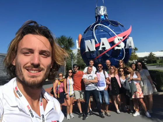 Eine WeRoad-Gruppe macht ein Selfie vor einem großen, blauen NASA-Logo unter klarem Himmel.