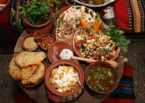 A traditional meal spread on a wooden surface, featuring various dishes in earthenware bowls, flatbread, and spices.