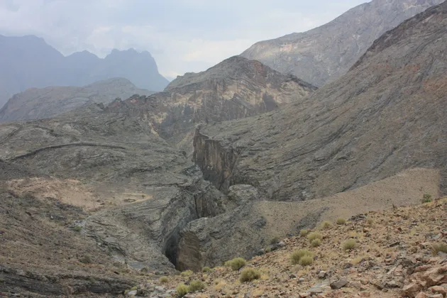 Un vaste paysage de montagnes rocheuses, traversé par un profond canyon, sous un ciel couvert.