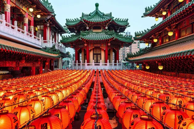 Des centaines de lanternes rouges illuminées, alignées devant un temple traditionnel est-asiatique aux toits de tuiles vertes.
