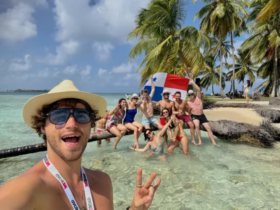 Un groupe WeRoad prend un selfie sur une plage tropicale, posant dans l'eau claire et tenant un drapeau panaméen.