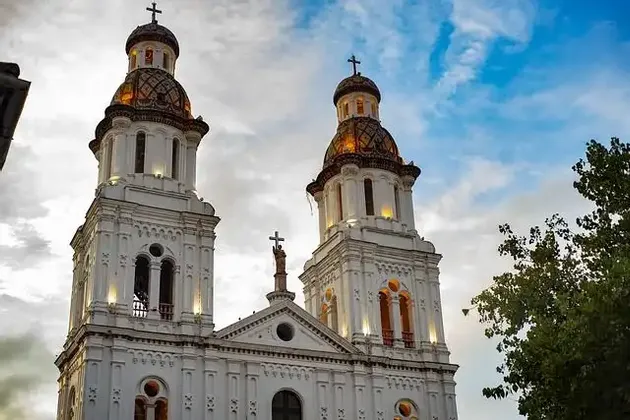 Le due torri bianche di una cattedrale con cupole piastrellate sono illuminate contro un cielo parzialmente nuvoloso.