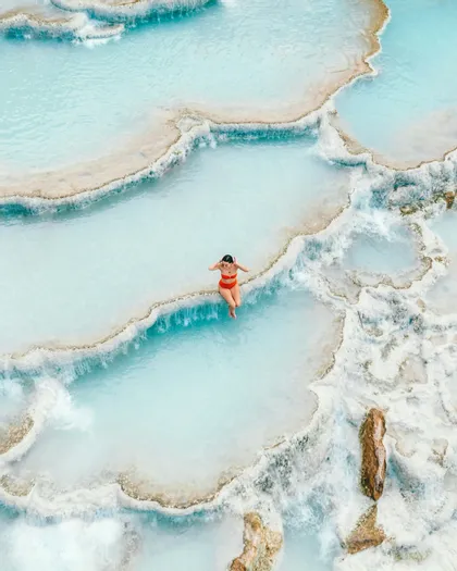 Vista aerea di una donna in bikini rosso che si rilassa in una serie di piscine termali terrazzate azzurre lattiginose.