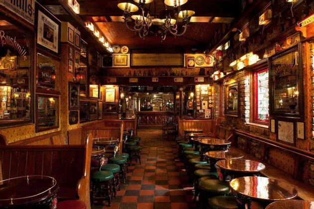L'interno accogliente di un pub classico con divanetti in legno scuro, tavoli rotondi, sgabelli verdi e un pavimento a scacchi.