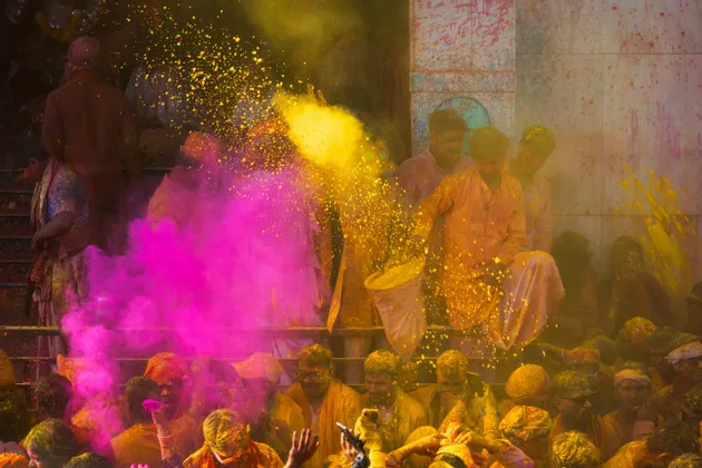 Una folla di persone a un festival lancia polvere gialla e rosa vibrante in aria.