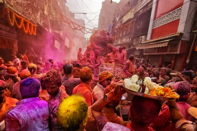 Una fitta folla di persone coperte di polveri colorate celebra il festival Holi in una stretta strada decorata.