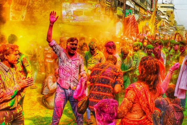 Una folla di persone celebra il festival Holi per strada, con i corpi e i vestiti coperti di polveri colorate.