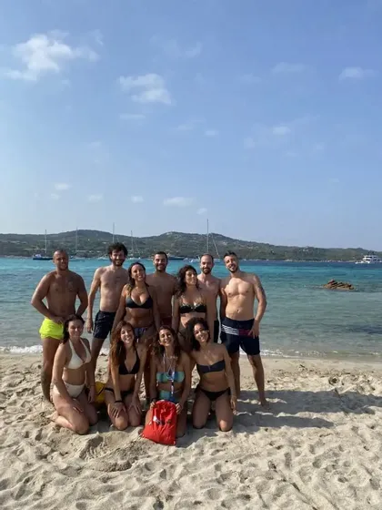 Un viaggio di gruppo WeRoad in costume da bagno, in posa su una spiaggia sabbiosa di fronte a un'acqua turchese con barche.
