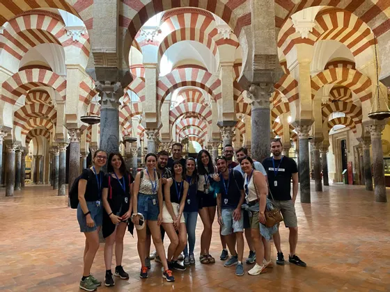 Un gruppo WeRoad in viaggio posa per una foto all'interno di un'ampia sala con caratteristici archi e colonne a strisce rosse e bianche.