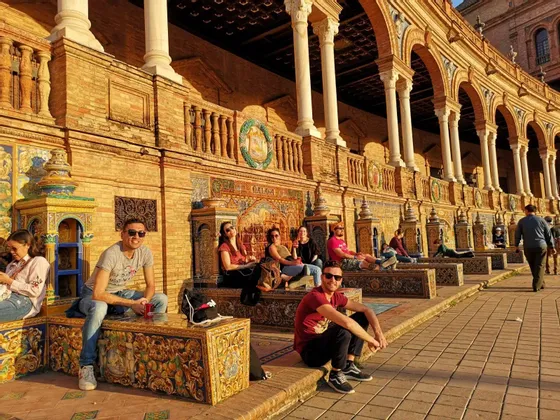 Un gruppo WeRoad in relax su panchine decorate e piastrellate di fronte a un edificio ad arco, all'ora d'oro.