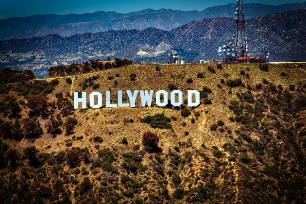 L'insegna bianca di Hollywood si erge su un'arida collina ricoperta di cespugli, con una torre di comunicazione nelle vicinanze e le montagne sullo sfondo.