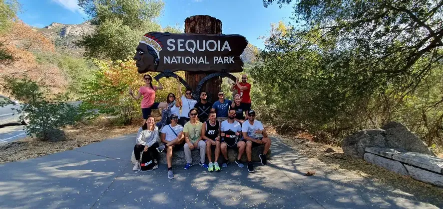 Un gruppo WeRoad in posa per una foto accanto al grande cartello di ingresso in legno del Sequoia National Park.