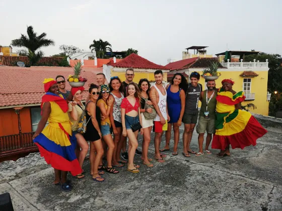 Un viaggio di gruppo WeRoad in posa per una foto su un tetto, con due donne in abiti tradizionali che trasportano cesti di frutta sulla testa.