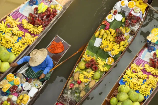 Luftaufnahme von Booten voller bunter tropischer Früchte wie Bananen und Ananas auf einem schwimmenden Markt.