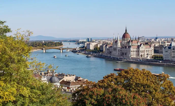 Una vista aerea della città mostra un grande edificio ornato sulla riva di un fiume, con barche e ponti sull'acqua.
