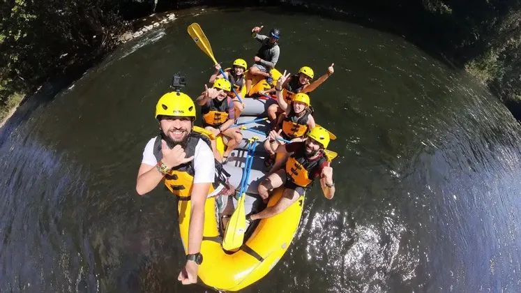 Ein Selfie aus der Vogelperspektive einer WeRoad-Gruppe, die lächelnd und posierend in einem gelben Schlauchboot einen Fluss hinuntertreibt.