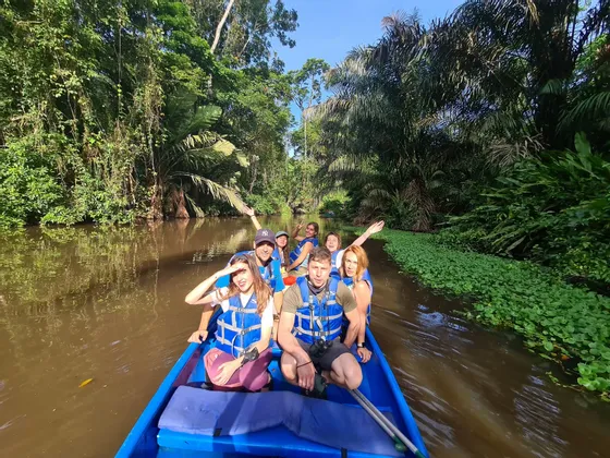 Eine WeRoad Gruppenreise befährt einen Dschungelfluss in einem blauen Boot, umgeben von dichter tropischer Vegetation.