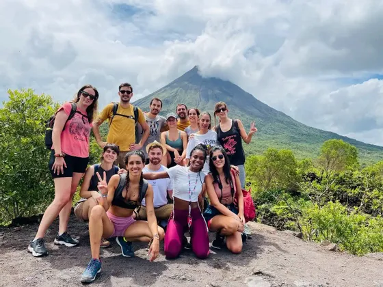 Un grupo de viaje de WeRoad sonríe y posa para una foto en una ruta de senderismo, con un gran volcán visible al fondo.