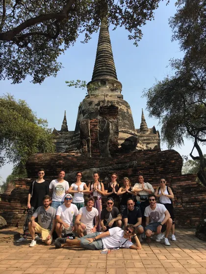 Eine WeRoad-Gruppe posiert für ein Foto vor einem alten Ziegeltempel mit einer hohen Stupa unter blauem Himmel.
