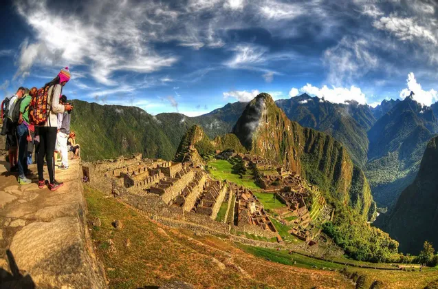 A WeRoad group trip looks out from a high vantage point over ancient stone ruins nestled in a green mountain valley.