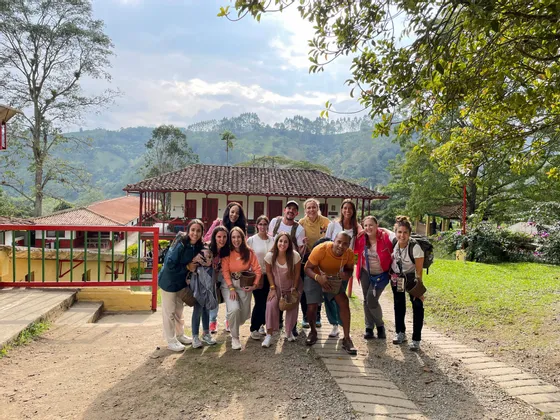 Un viaje en grupo de WeRoad posa para una foto en un sendero frente a un edificio rural, con exuberantes colinas verdes de fondo.