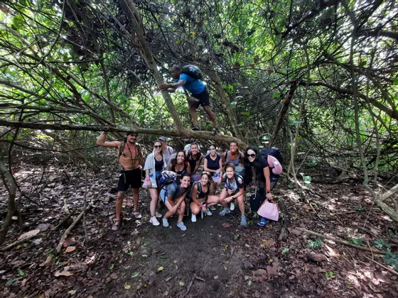 Un viaje en grupo de WeRoad con mochilas posa para una foto en un sendero bajo ramas de árboles enredadas en un bosque denso.