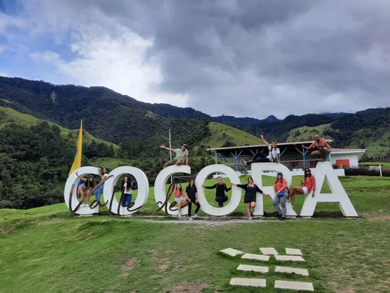 Un viaje en grupo de WeRoad posando para una foto en el gran cartel blanco del 'Valle de Cocora' con un telón de fondo de montañas verdes.