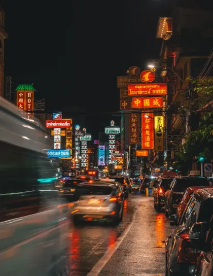 Une rue de ville animée la nuit, remplie de circulation automobile, illuminée par des néons colorés se reflétant sur le pavé mouillé.