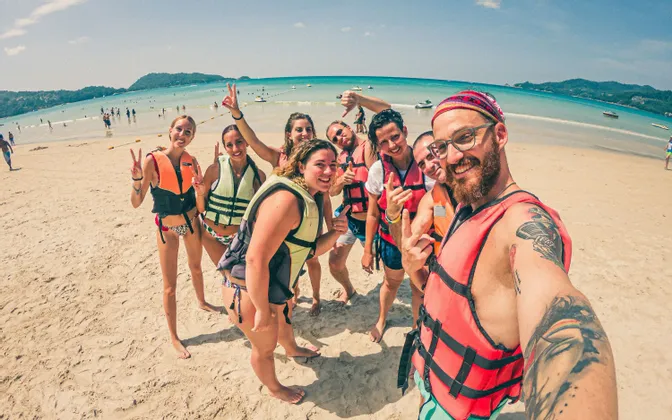Eine WeRoad Gruppe mit Schwimmwesten posiert für ein Selfie an einem Sandstrand, mit dem Meer im Hintergrund.