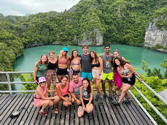 Eine WeRoad-Gruppenreise posiert für ein Foto auf einem hölzernen Aussichtspunkt mit Blick auf eine türkise Lagune, umgeben von üppig grünen Klippen.