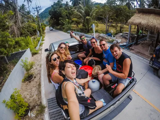 Eine WeRoad-Gruppe macht ein Selfie auf der Ladefläche eines Pick-ups auf einer von Palmen gesäumten Straße.