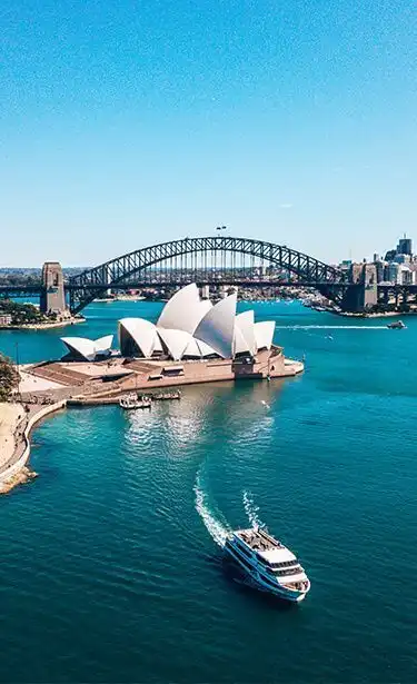 Vista aerea dell'Opera House di Sydney e dell'Harbour Bridge, con un traghetto che solca le acque azzurre.