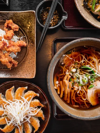 Una vista dall'alto di un pasto giapponese con una ciotola di ramen, un piatto di karaage e ravioli gyoza su un tavolo scuro.