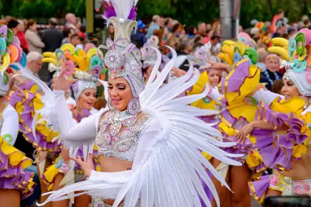 Una donna in un costume di carnevale bianco e ingioiellato con piume balla durante una sfilata di strada con altri artisti.
