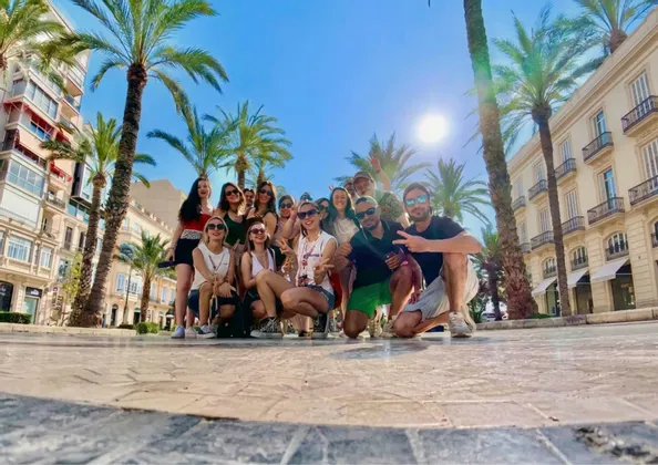 Un gruppo WeRoad si fa fotografare dal basso in una piazza assolata, circondata da alte palme ed edifici storici.